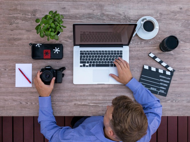 man working on laptop, coffee, camera, notepad