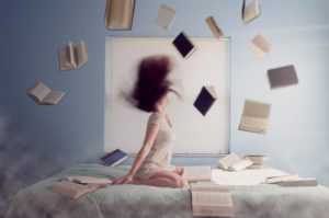 woman sitting on bed with flying books - lacie-slezak-yHG6llFLjS0-unsplash